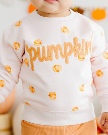 Baby wearing pink crewneck sweatshirt with pumpkin pattern and patch that reads 'pumpkin'