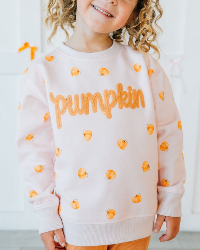 Girl wearing pink crewneck sweatshirt with pumpkin pattern and patch that reads 'pumpkin'