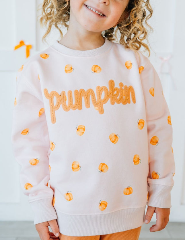 Girl wearing pink crewneck sweatshirt with pumpkin pattern and patch that reads 'pumpkin'