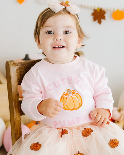 Baby wearing a long sleeve pink baby romper with pumpkin patch and text 'cutest pumpkin'