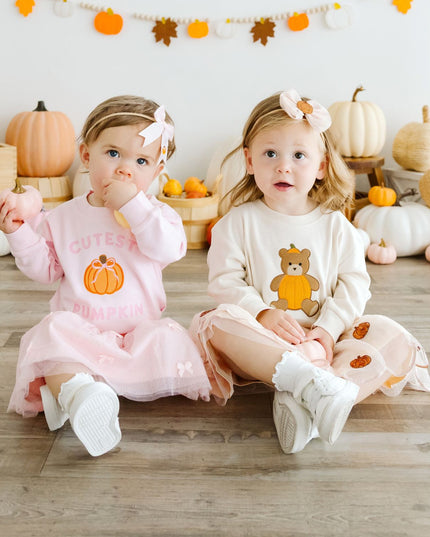 Two babies sitting wearing coordinating pumpkin outfits
