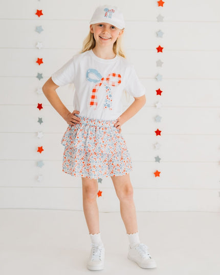 Girl wearing white t-shirt with a patchwork bow design featuring red, white, and blue colors and floral skirt