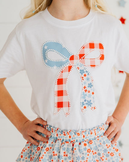 Girl wearing white t-shirt with a patchwork bow design featuring red, white, and blue colors and floral skirt