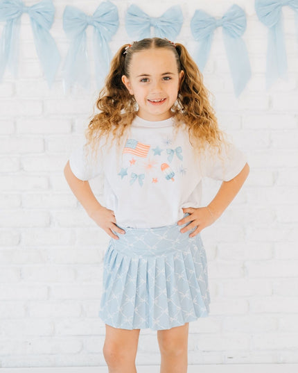 Girl wearing white t-shirt with red, white and blue graphic design and blue skort