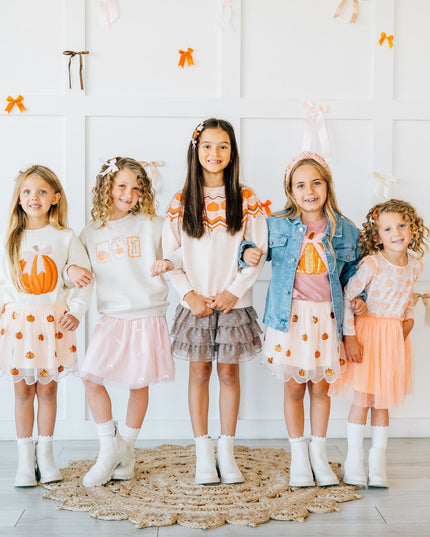 5 girls standing wearing matching outfits with pumpkins.