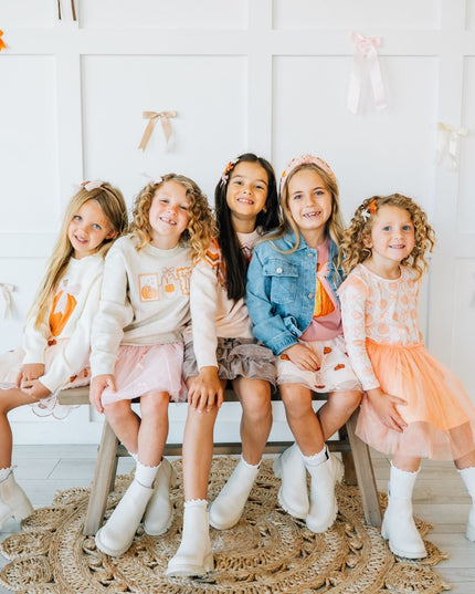 five girls sitting wearing matching outfits with pumpkins.
