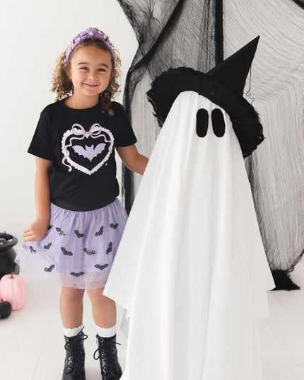 A girl wearing a black shirt with a bat and a purple tulle tutu skirt with black sequin bats 
