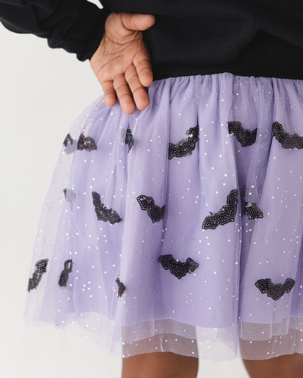 A girl wearing a purple tulle tutu skirt with black sequin bats 