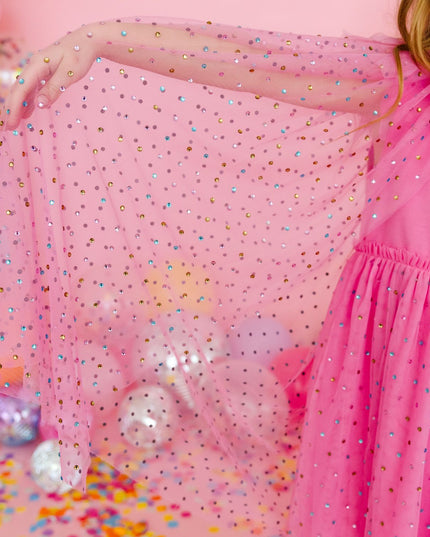 Girl wearing pink dress holding out  pink tulle cape with multicolor rhinestones