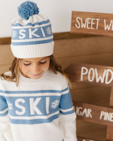 Girl wearing white and blue pom-pom 'ski'  beanie and sweater