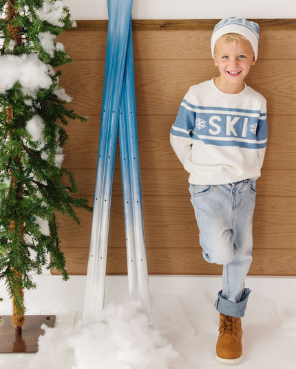 Boy wearing white and blue pom-pom 'ski'  beanie and sweater