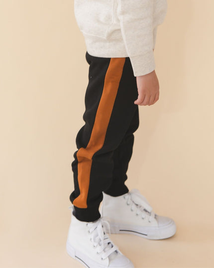 Boy wearing black jogger pants with burnt orange  side stripes