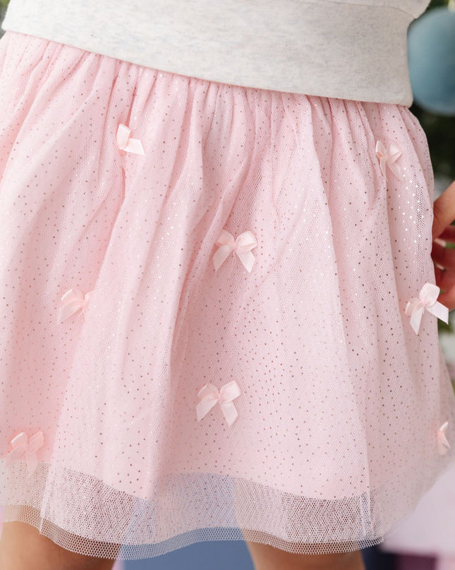 A girl wearing a light pink tulle tutu skirt with small bow embellishments