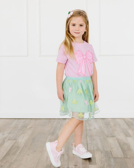 Girl wearing pink t-shirt with oversized sequin bow patch and green skirt