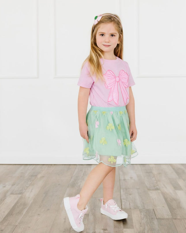 Girl wearing pink t-shirt with oversized sequin bow patch and green skirt