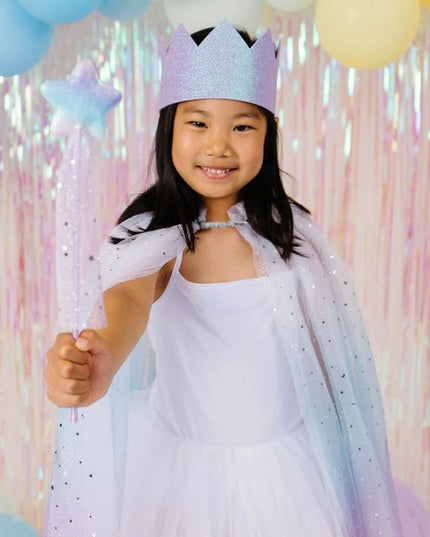 A young girl posing in a sparkly lavender-blue cape, matching tiara, and heart-shaped sunglasses