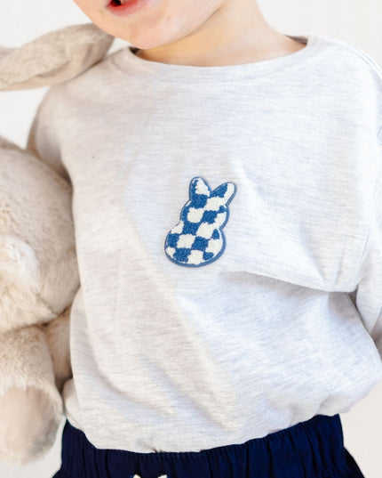 Boy wearing ash grey t-shirt with blue and white bunny checkered patch holding a stuffed bunny