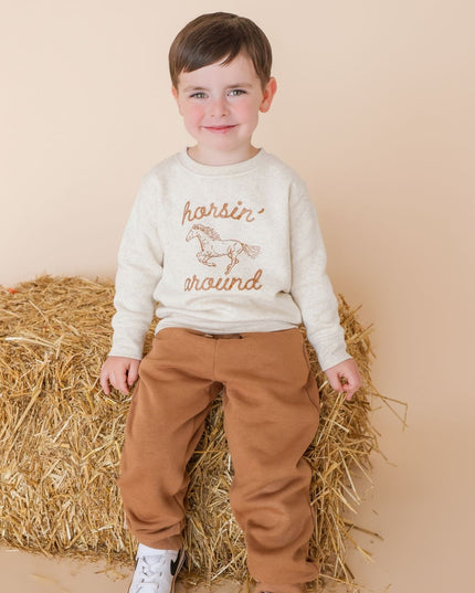 Boy wearing sweatshirt with 'horsin' around' graphic and brown pants