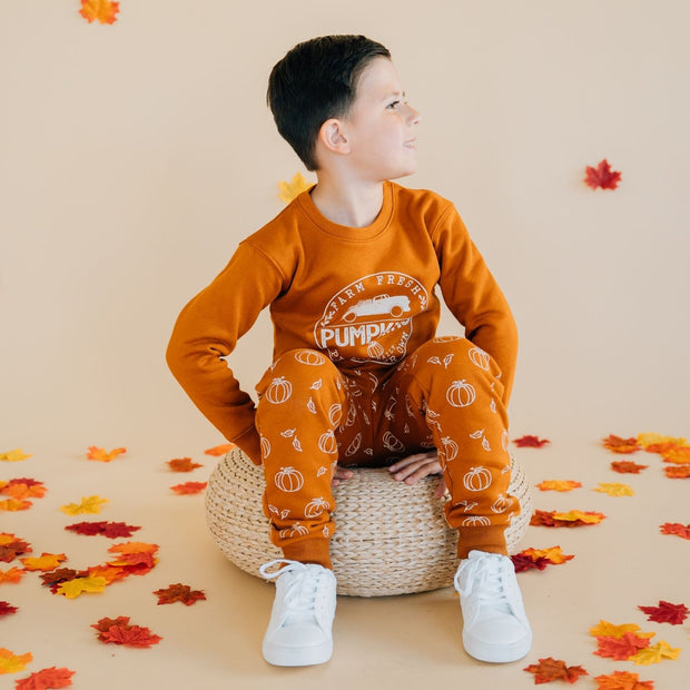 Boy sitting wearing Burnt orange sweatshirt with pumpkin truck graphic and pumpkin sweatpants