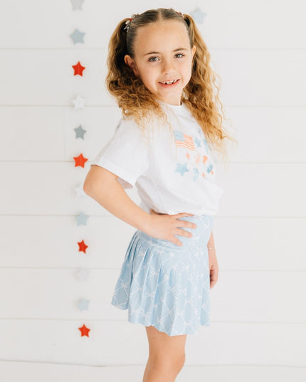 Girl wearing white t-shirt with red, white and blue graphic design and blue skort