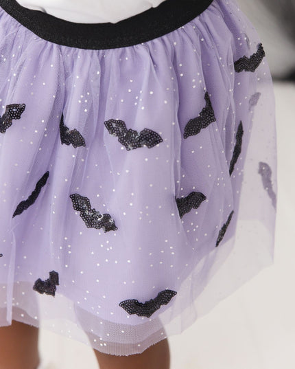 A girl wearing a purple tulle tutu skirt with black sequin bats 