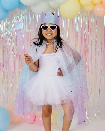 A young girl posing in a sparkly lavender-blue cape, matching tiara, and heart-shaped sunglasses