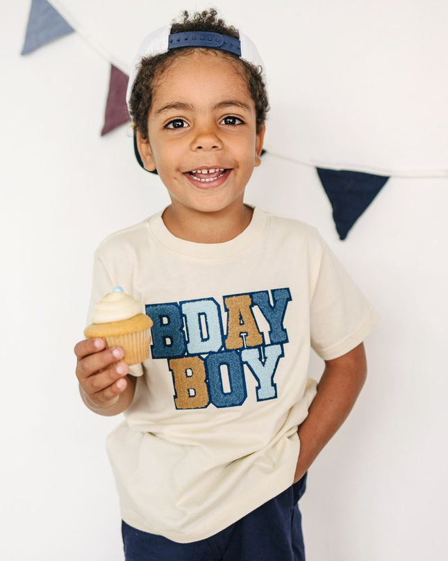 Boy wearing a 'BDAY BOY' shirt holding a cupcake.