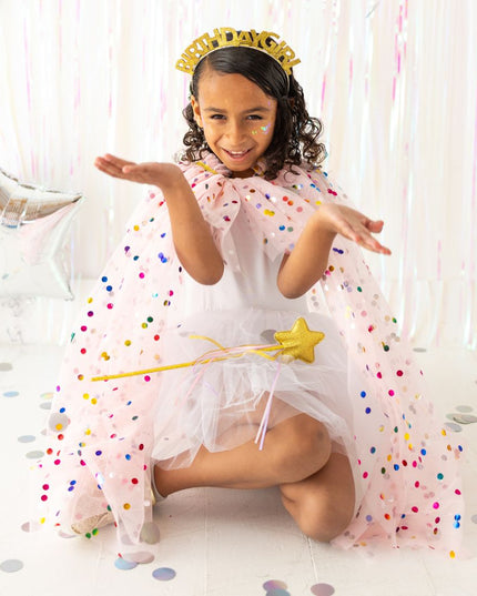 Girl sitting wearing pink polka dot cape with gold birthday girl headband