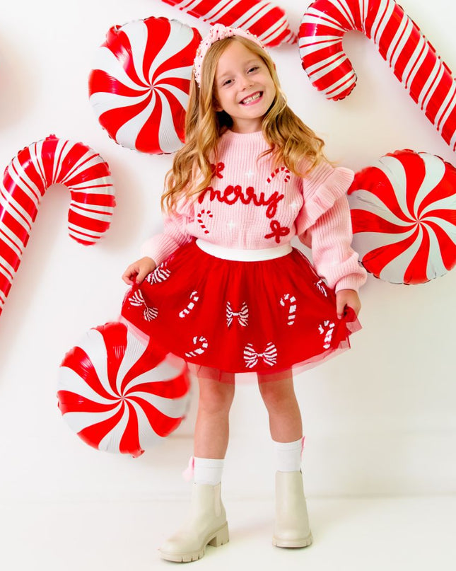 Girl wearing red tutu with red and white sequin candy canes and bows and pink merry sweater 
