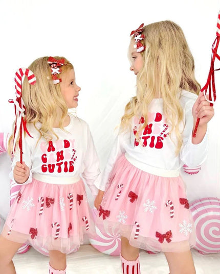 two girls wearing Christmas outfits holding candy cane Christmas wands
