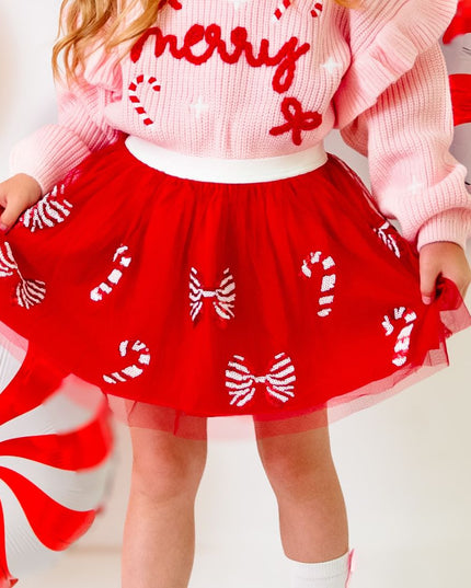 Girl wearing red tutu with red and white sequin candy canes and bows and pink merry sweater 