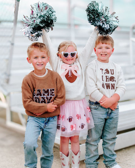 Kids wearing festive game day football outfits in front of bleachers