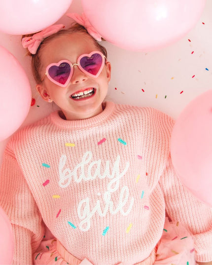 Girl wearing a pink sweater embroidered with 'bday girl', surrounded by pink balloons and sprinkles.
