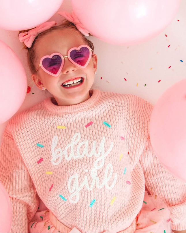 Girl wearing a pink sweater embroidered with 'bday girl', surrounded by pink balloons and sprinkles.