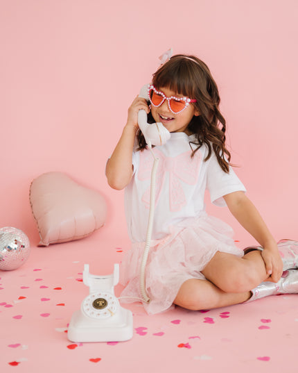 Girl wearing white t-shirt with pink lace bow talking on the phone