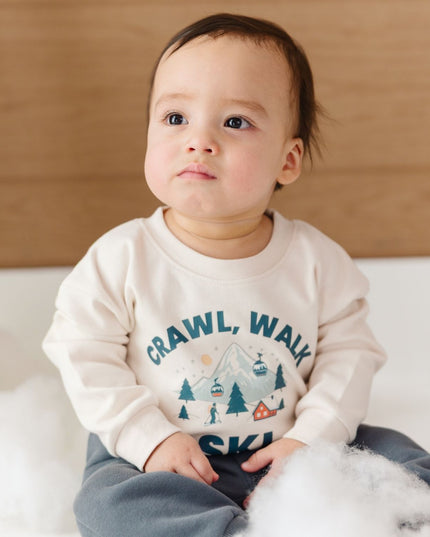 Baby sitting wearing an off-white crawl, walk ski graphic romper and slate grey jogger pants