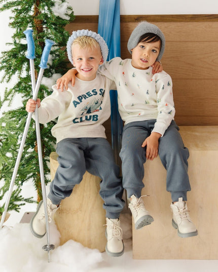 Two boys sitting wearing ski themed sweatshirts and slate grey jogger pants