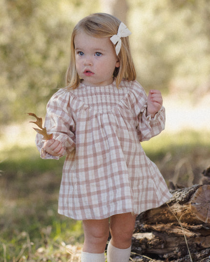 A toddler wearing a long-sleeve smocked dress with a rustic plaid pattern