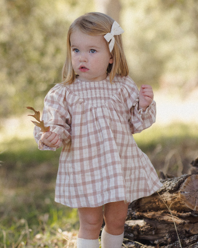 A toddler wearing a long-sleeve smocked dress with a rustic plaid pattern