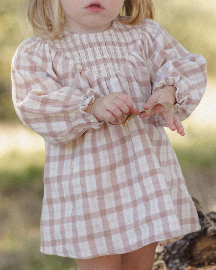 A toddler wearing a long-sleeve smocked dress with a rustic plaid pattern