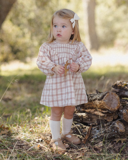 A toddler wearing a long-sleeve smocked dress with a rustic plaid pattern