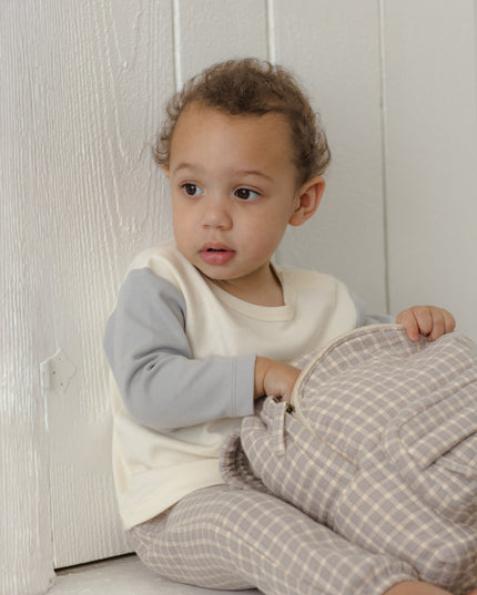 Boy sitting wearing long sleeve children's white raglan tee with grey sleeves and grey plaid pants