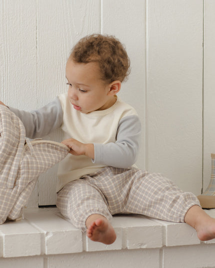 Boy sitting wearing long sleeve children's white raglan tee with grey sleeves and grey plaid pants