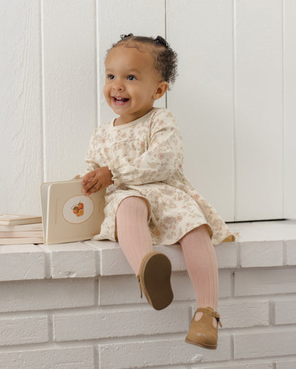 Toddler reading a book wearing a long-sleeve dress with a tiered ruffle hem and floral pattern with pink tights