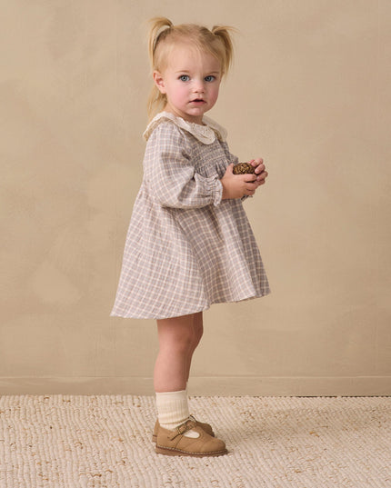 A little girl wearing a long sleeve dress with blue checkered pattern and white collar 