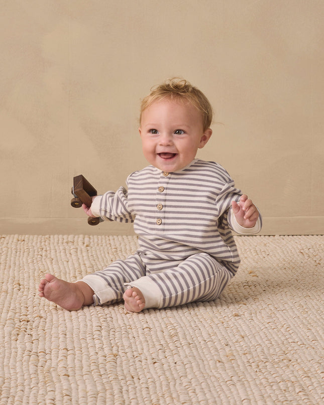 Baby sitting wearing a slate grey and white striped jumpsuit