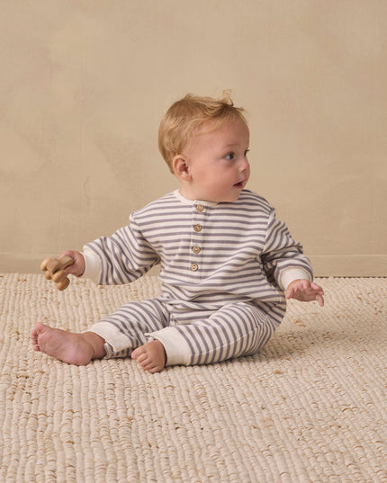 Baby sitting wearing a slate grey and white striped jumpsuit