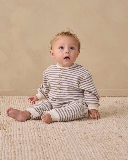 Baby sitting wearing a slate grey and white striped jumpsuit