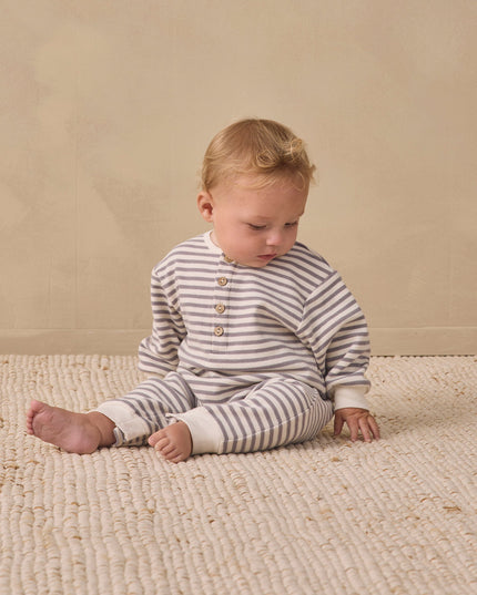 Baby sitting wearing a slate grey and white striped jumpsuit