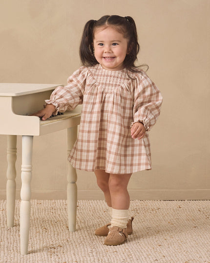 A toddler wearing a long-sleeve smocked dress with a rustic plaid pattern